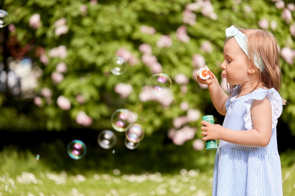 childhood, leisure and people concept - little girl blowing soap bubbles at summer park or garden. little girl blowing soap bubbles at park or garden