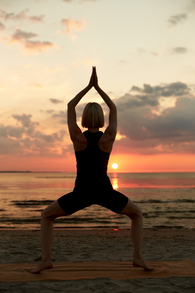 fitness, sport, and healthy lifestyle concept - woman doing yoga goddess pose on beach over sunset. woman doing yoga goddess pose on beach