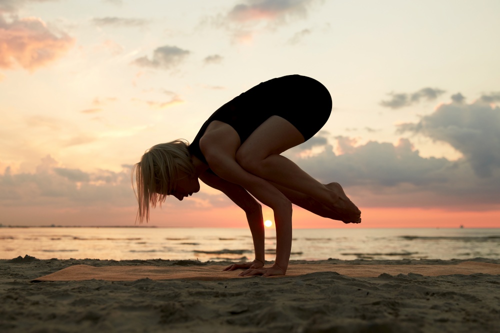 fitness, sport, and healthy lifestyle concept - woman doing yoga crow pose on beach over sunset. woman doing yoga crow pose on beach over sunset