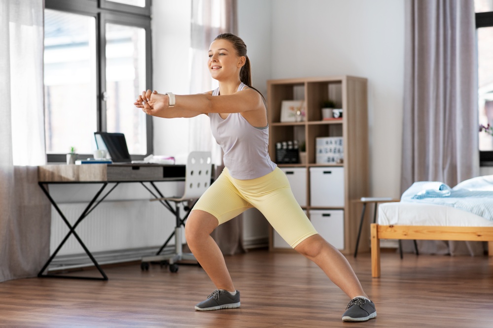 sport, fitness and healthy lifestyle concept - smiling teenage girl exercising and stretching leg at home. happy teenage girl exercising at home