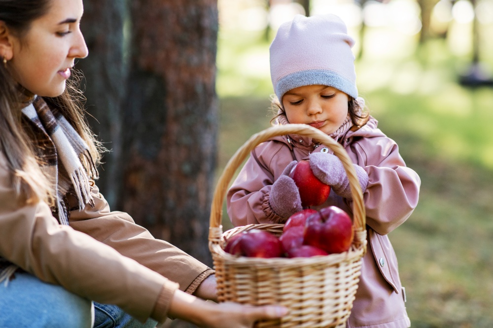 family, leisure and people concept - mother and baby daughter with apples in wicker basket at park. mother and baby daughter with basket of apples