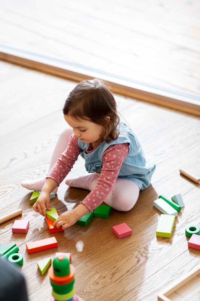 childhood, leisure and people concept - little baby girl playing with wooden toy blocks on floor at home. happy baby girl playing with toy blocks at home