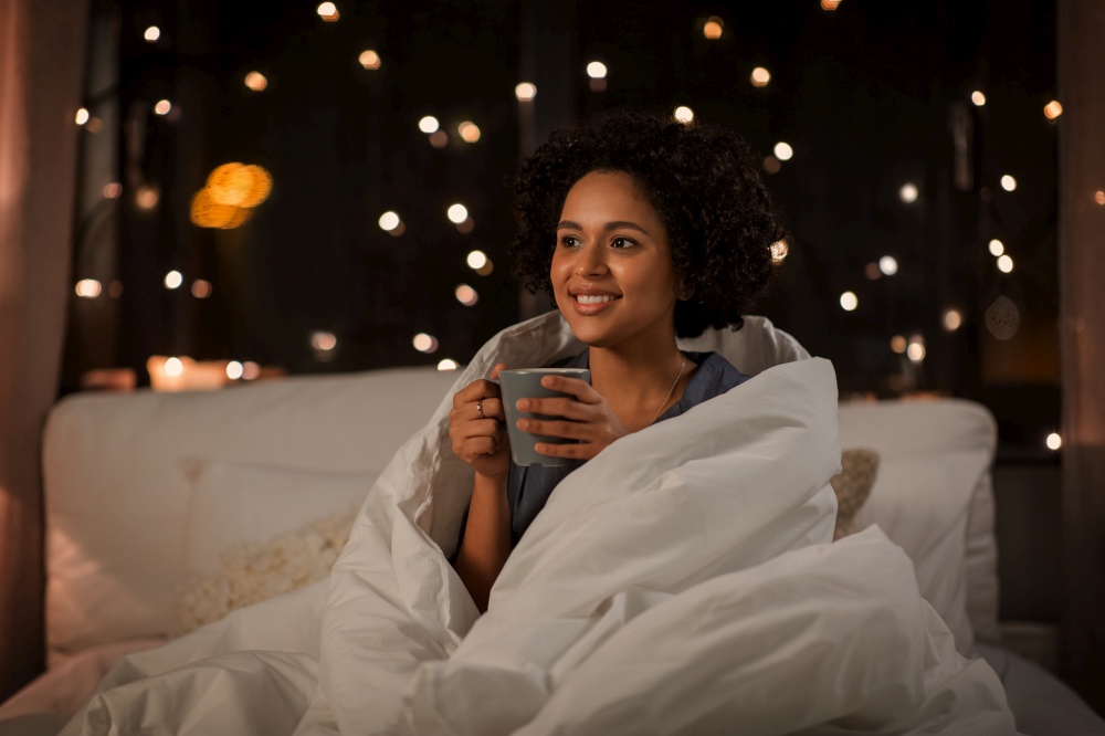people, bedtime and rest concept - happy smiling woman in pajamas with coffee sitting in bed at night. happy woman with coffee sitting in bed at night