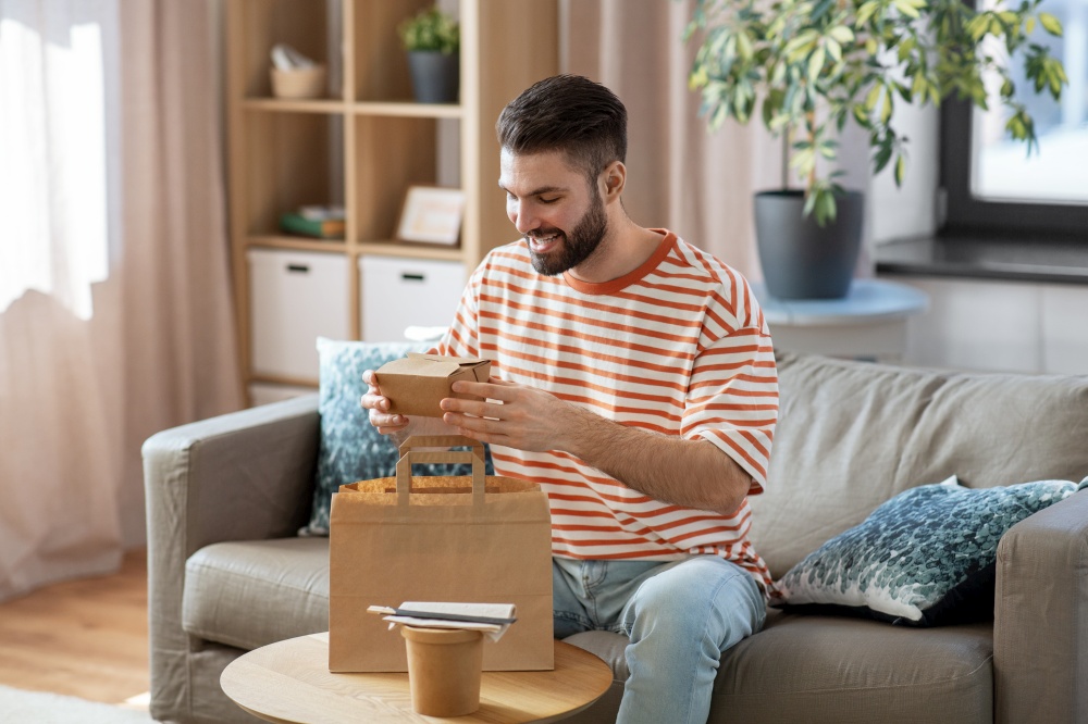 consumption, eating and people concept - smiling man unpacking takeaway food in paper bag at home. smiling man unpacking takeaway food at home