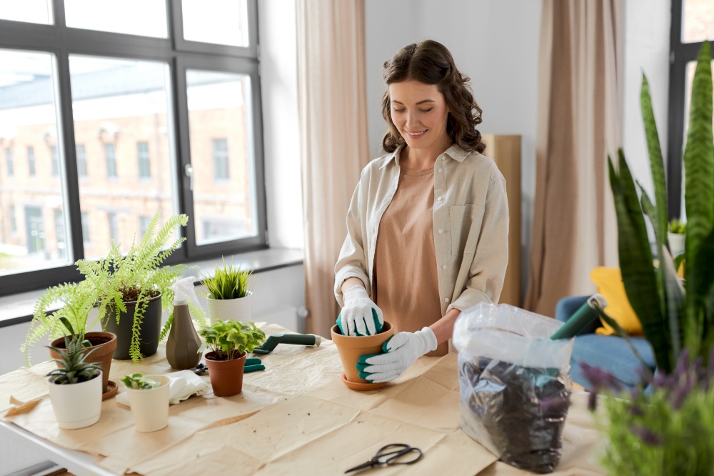 people, gardening and housework concept - happy woman in gloves planting pot flowers at home. happy woman planting pot flowers at home