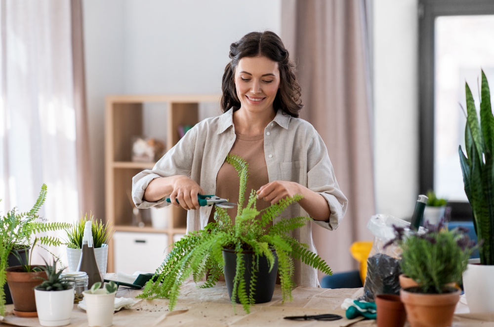people, gardening and housework concept - happy woman cutting fern flower&rsquo;s leaves with pruner at home. woman cutting flower&rsquo;s leaves with pruner at home