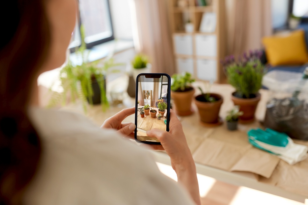 people, gardening and housework concept - close up of woman with smartphone photographing pot flowers at home. woman with smartphone photographing pot flowers