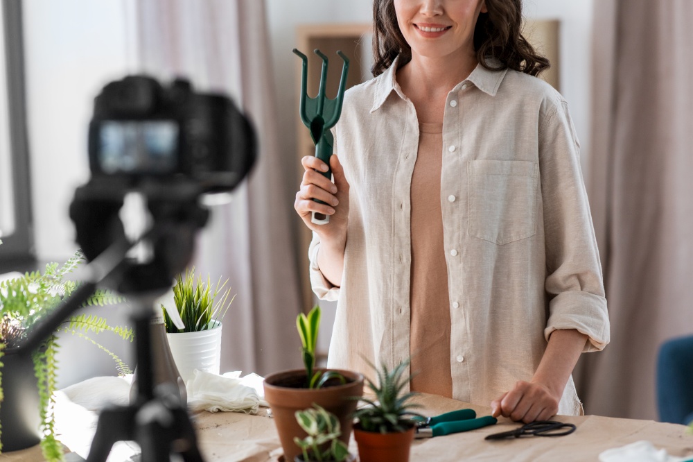 blogging, gardening and housework concept - happy woman or blogger with camera and fork planting pot flowers and recording tutorial video at home. happy woman or blogger planting flowers at home