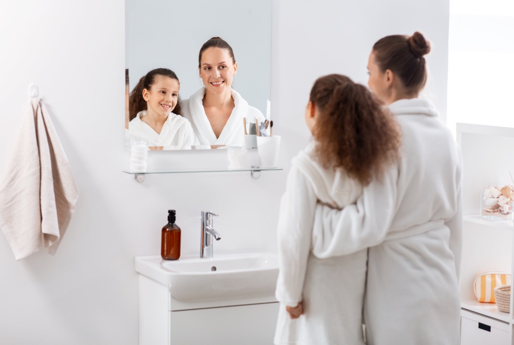 beauty, hygiene, morning and people concept - happy smiling mother and daughter looking to mirror at bathroom. mother and daughter looking to mirror at bathroom