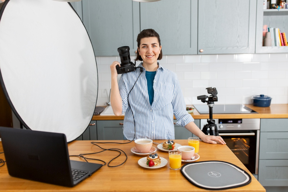 blogging, profession and people concept - happy smiling female food photographer with camera photographing pancakes, coffee and orange juice in kitchen at home. food photographer with camera working in kitchen