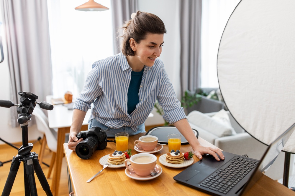 blogging, photographing and people concept - happy smiling female food blogger or photographer with laptop and camera in kitchen at home. female food photographer with laptop in kitchen