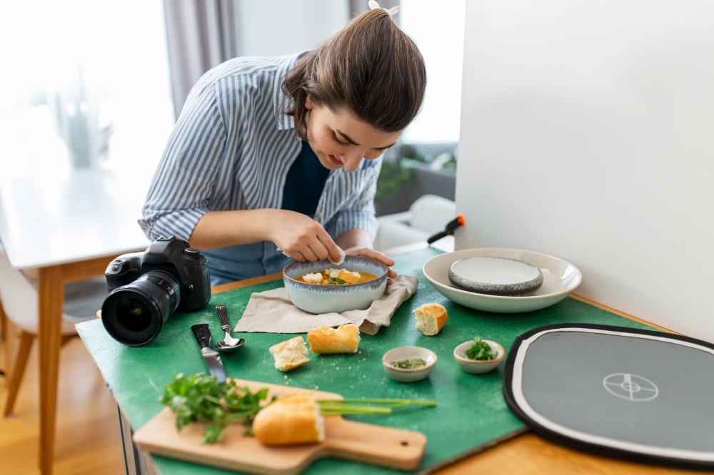 blogging, photographing and people concept - happy smiling female food photographer with camera arranging composition in kitchen at home. food photographer arranging composition in kitchen