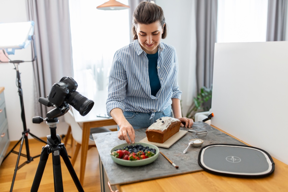 blogging, photographing and people concept - happy smiling female photographer or food blogger with camera, cake and berries working in kitchen at home. food blogger with camera working cake in kitchen