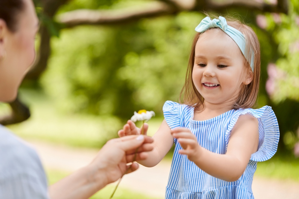 family, motherhood and people concept - happy mother and little daughter with chamomile flower at summer park or garden. happy mother and daughter with flower at park