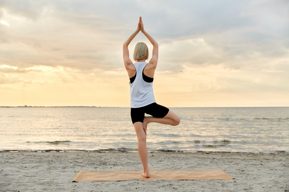 fitness, sport, and healthy lifestyle concept - woman doing yoga tree pose on beach over sunset. woman doing yoga tree pose on beach over sunset