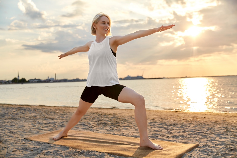 fitness, sport, and healthy lifestyle concept - happy woman doing yoga warrior pose on beach over sunset. happy woman doing yoga warrior pose on beach