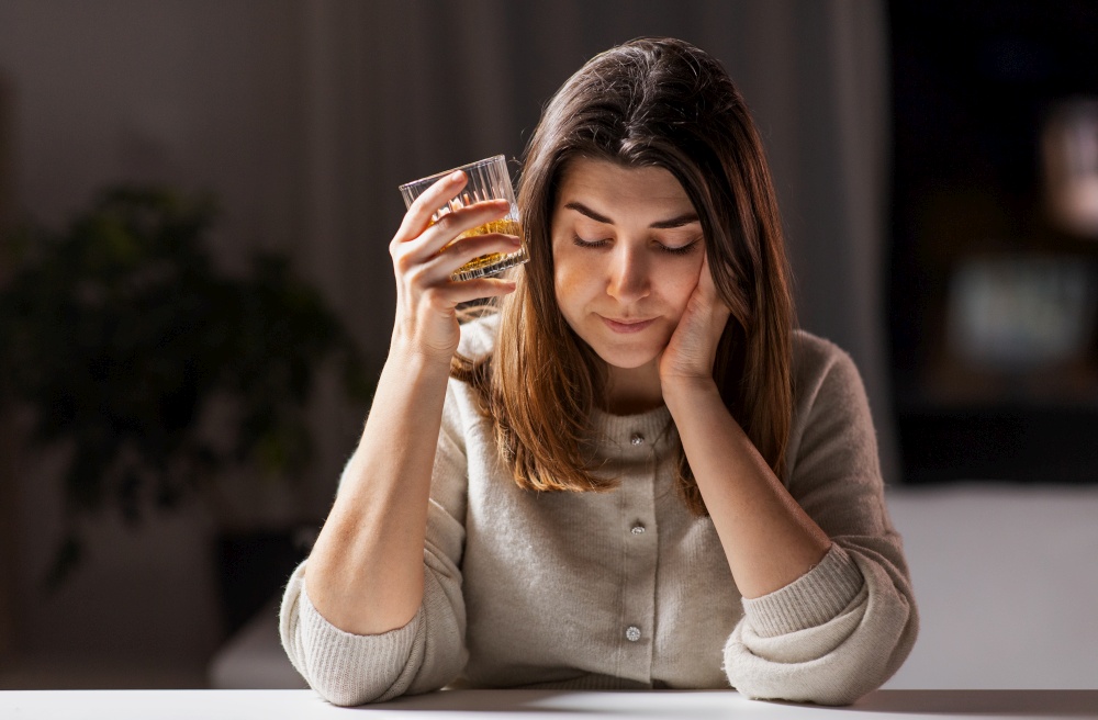 alcoholism, alcohol addiction and people concept - drunk woman or female alcoholic drinking whiskey at home. woman alcoholic drinking strong alcohol at home