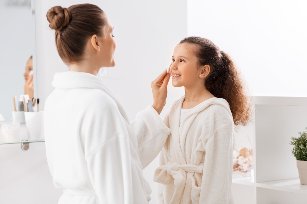 beauty, hygiene, morning and people concept - happy smiling mother with cotton pad cleaning daughter&rsquo;s face skin at bathroom. mother with cotton pad cleaning daughter&rsquo;s face