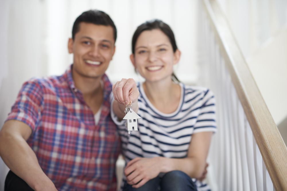 Young Couple Sitting On Stairs Holding Keys To New Home