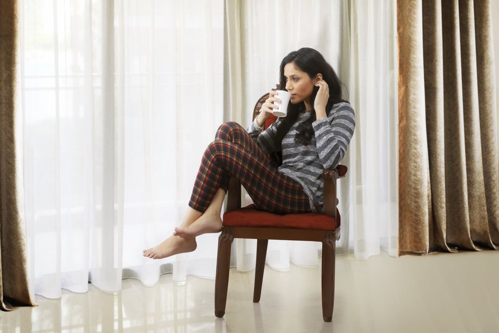 Woman drinking coffee and relaxing on armchair looking out from window