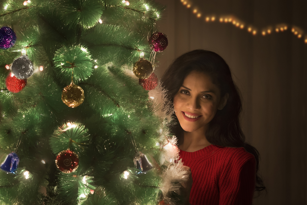 Young woman decorating Christmas tree looking at camera