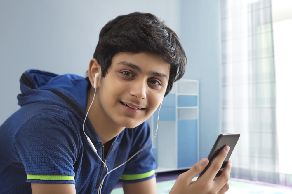 PORTRAIT OF A TEENAGER LOOKING AT CAMERA WHILE HOLDING MOBILE PHONE