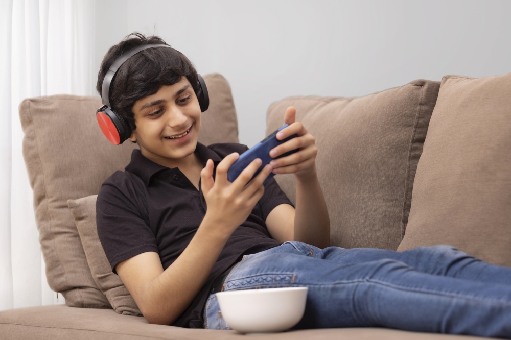 A HAPPY TEENAGER PLAYING VIDEO GAME ON MOBILE WHILE RESTING ON SOFA