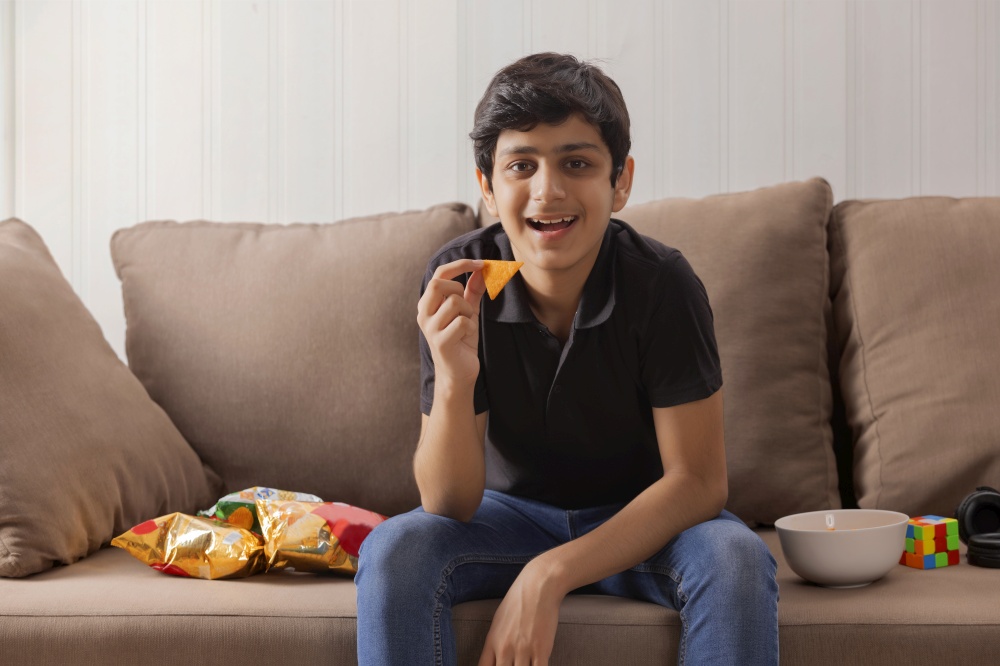 A HAPPY TEENAGER SITTING AND EATING SNACKS WHILE AT HOME