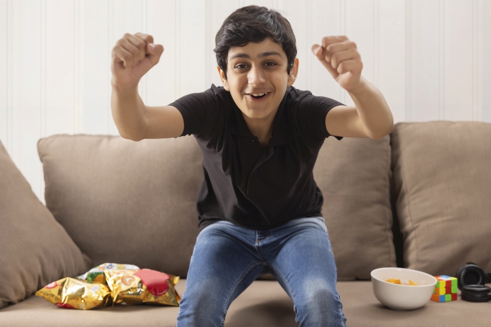 A TEENAGE BOY EXCITEDLY LOOKING AT CAMERA WHILE EATING SNACKS