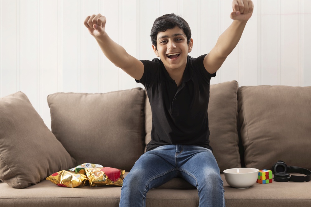 A TEENAGE BOY HAPPILY CHEERING WHILE SITTING IN FRONT OF CAMERA