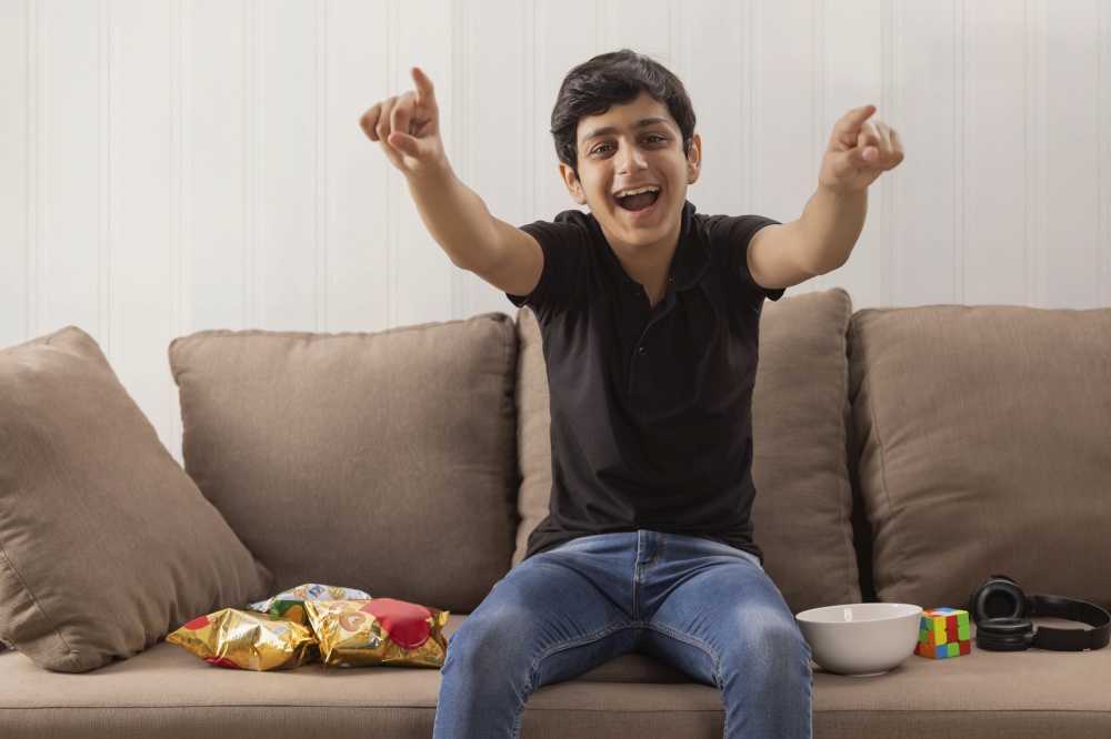 A HAPPY TEENAGE BOY CHEERING WHILE ENJOYING AT HOME