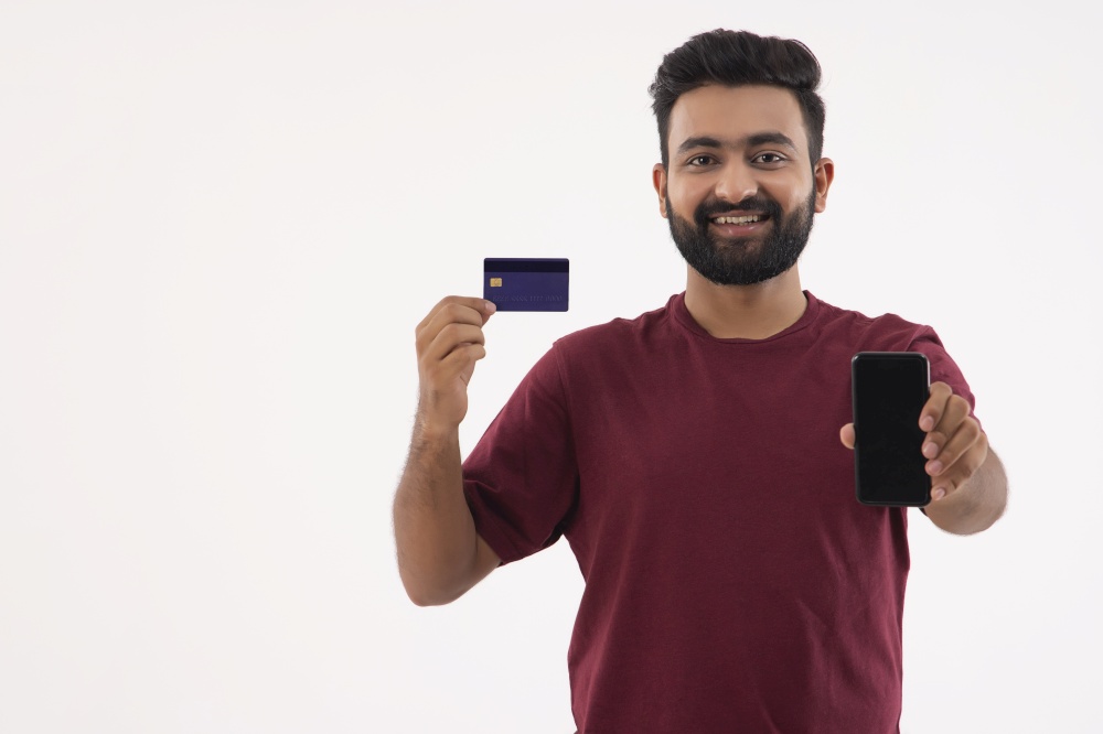 A YOUNG BEARDED MAN POSING WITH DEBIT CARD AND MOBILE PHONE IN HAND