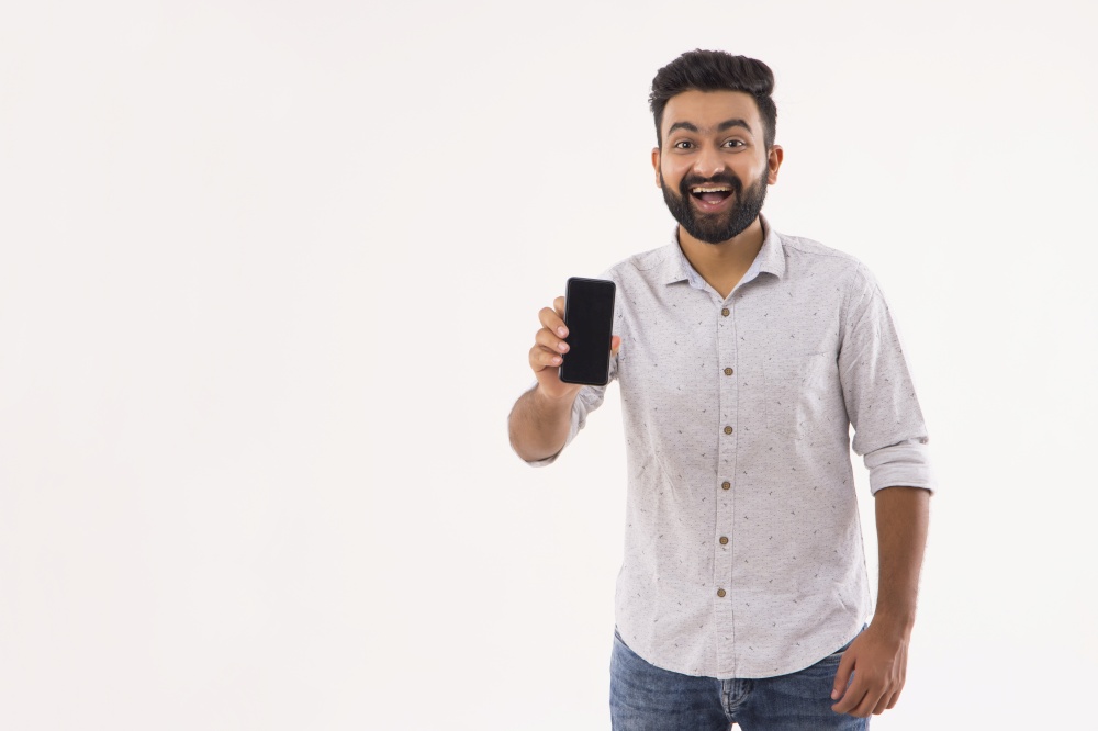 A BEARDED YOUNG MAN LAUGHING AND SHOWING MOBILE IN FRONT OF CAMERA