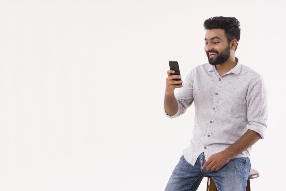 A BEARDED YOUNG MAN LOOKING SURPRISED WHILE USING MOBILE