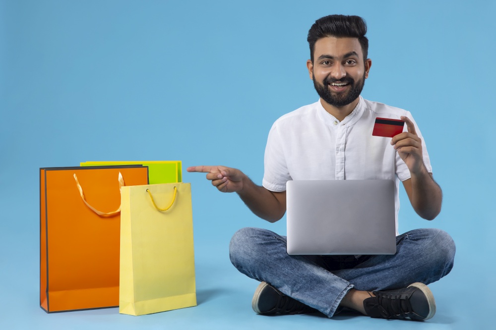 A HAPPY YOUNG MAN POINTING AT SHOPPING BAGS WHILE HOLDING DEBIT CARD