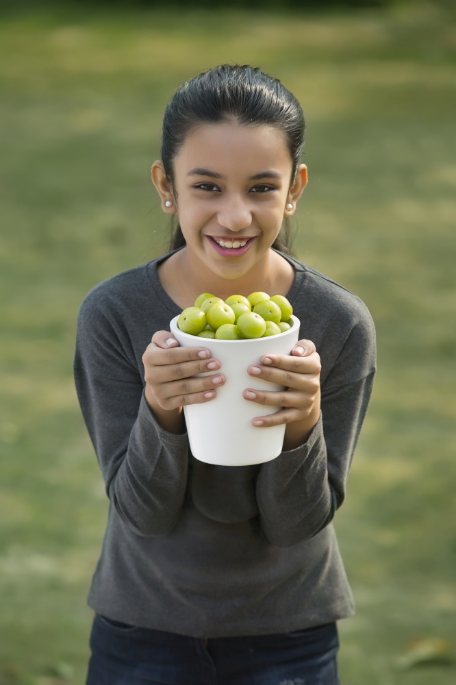 Portrait of a smiling young girl holding a jar full of indian gooseberries or amla.