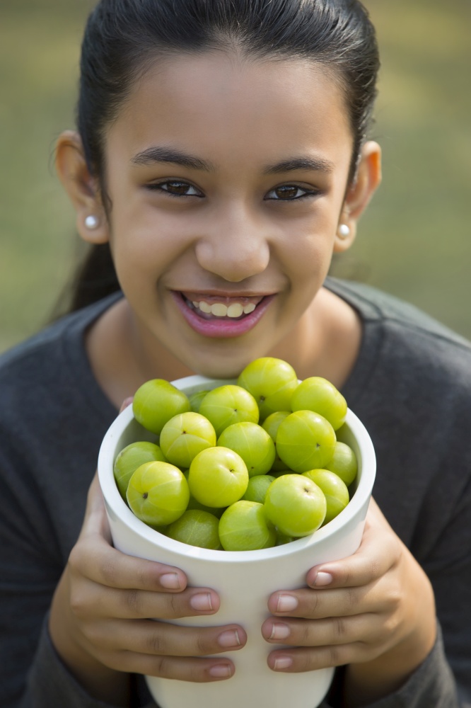 Close up of a smiling young girl holding a jar full of indian gooseberries or amla.