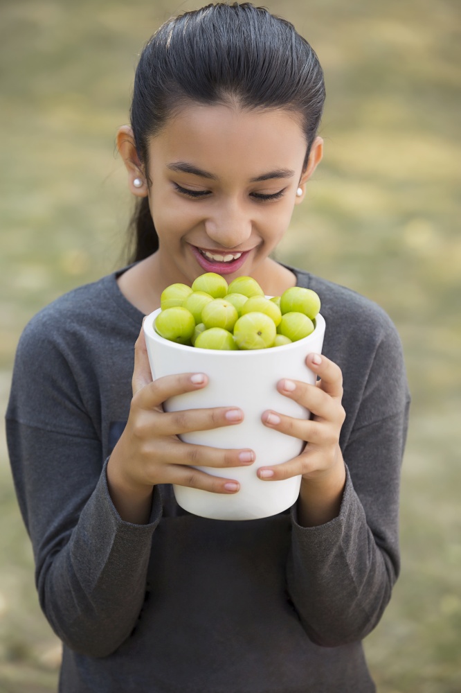 Close up of a smiling young girl looking at the jar full of indian gooseberries or amla that she is holding.