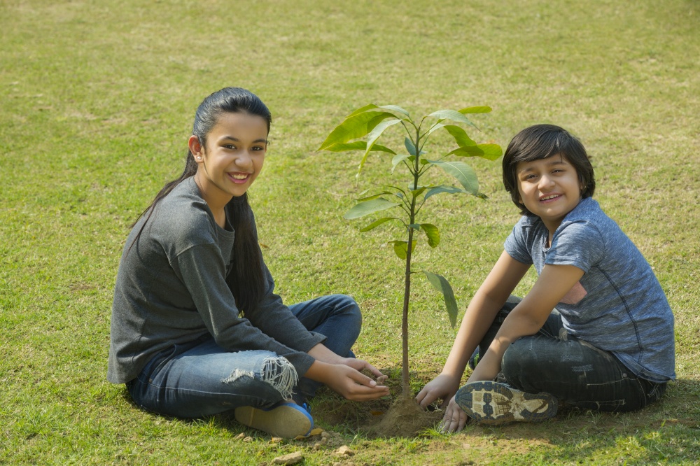 Smiling young boy and girl planting a small plant in garden sitting on the ground.