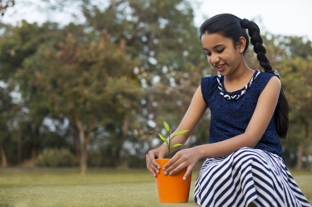 Young girl planting a sapling in a small flower pot sitting in a park.