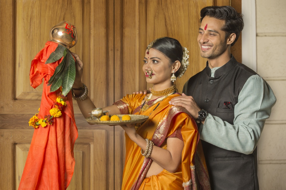 Happy maharashtrian couple in traditional dress celebrating gudi padwa festival holding a pooja plate.