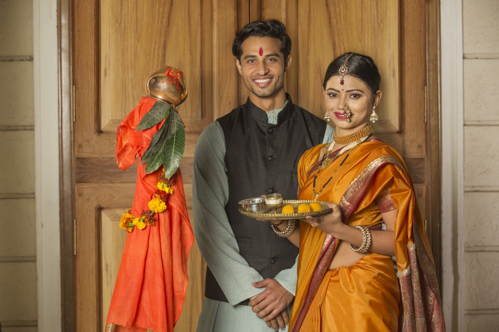 Happy maharashtrian couple in traditional dress celebrating gudi padwa festival holding a pooja plate and posing.