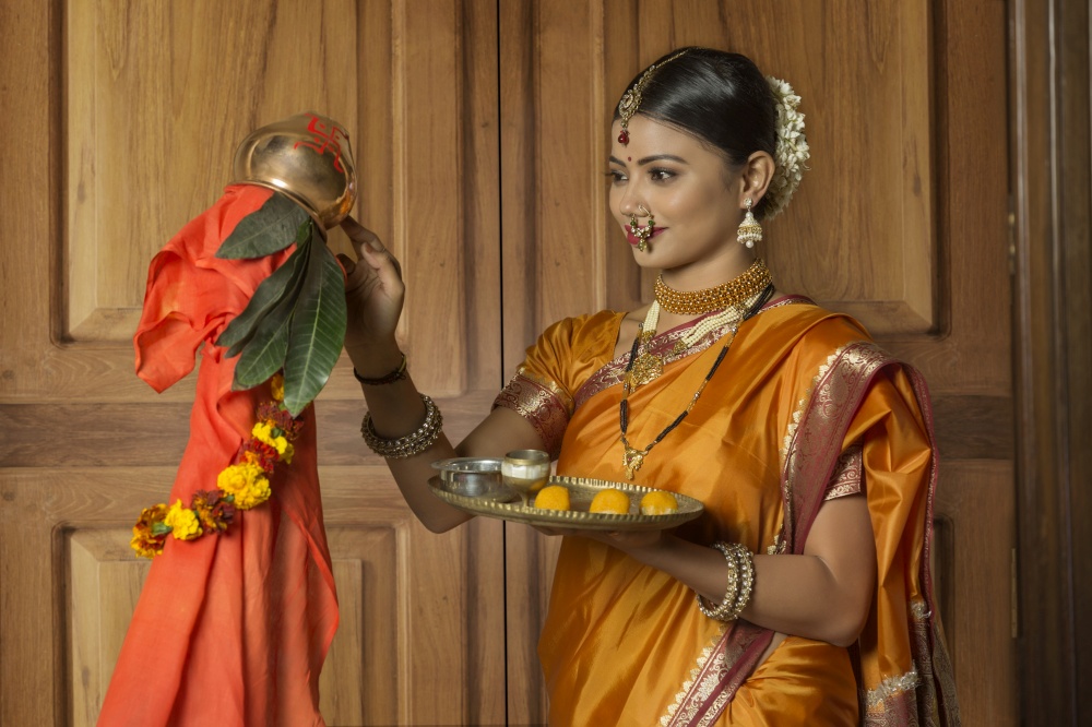 Maharashtrian woman in traditional dress celebrating gudi padwa festival applying tilak on gudi holding a pooja plate.