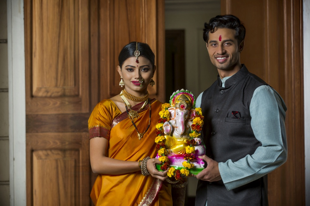 Maharashtrian couple in traditional dress celebrating ganapati festival holding a small statue of lord ganesha together.