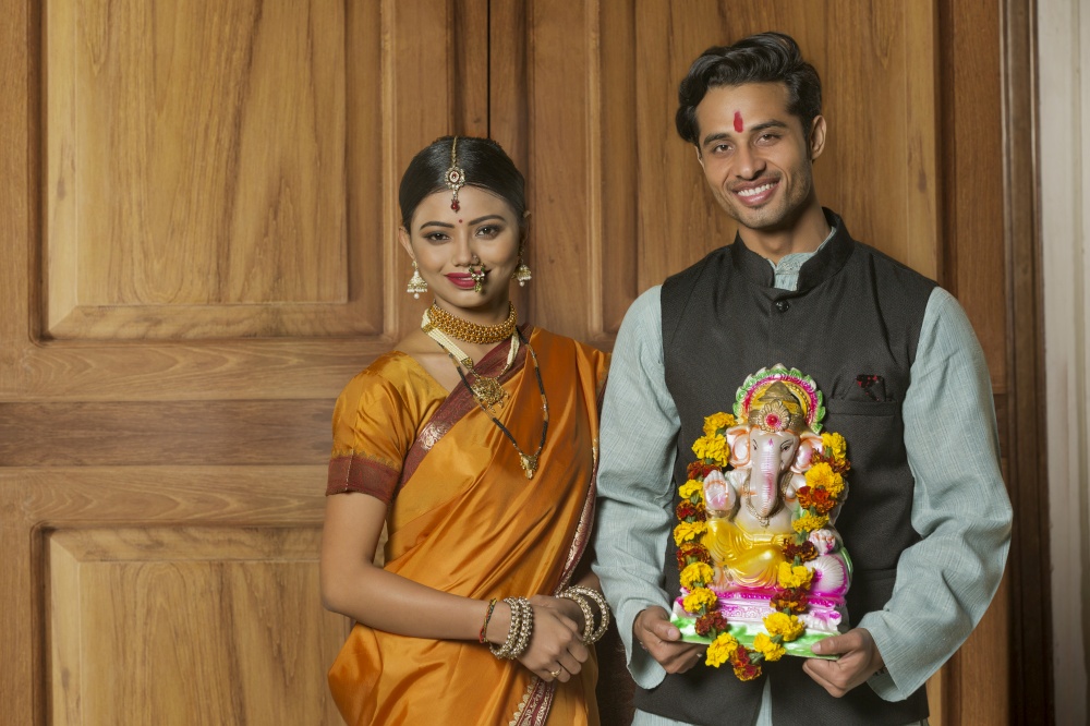 Happy maharashtrian couple in traditional dress celebrating ganapati festival holding a small statue of lord ganesha.