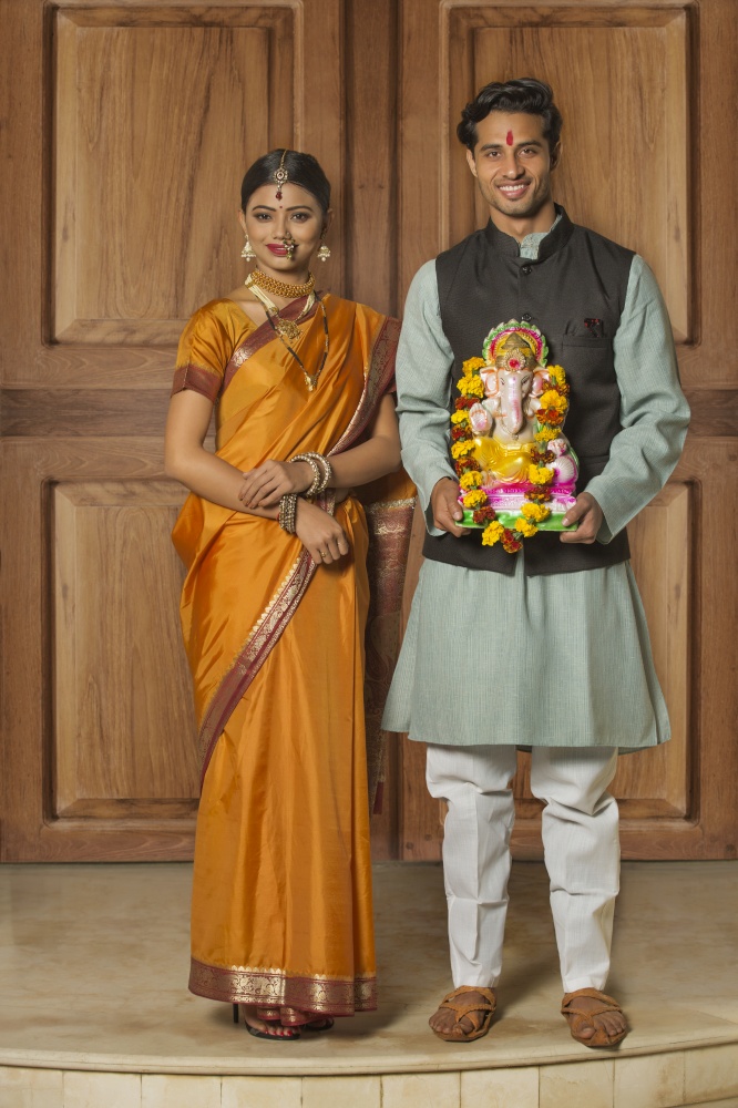 Portrait of happy maharashtrian couple in traditional dress celebrating ganapati festival holding a small statue of lord ganesha.