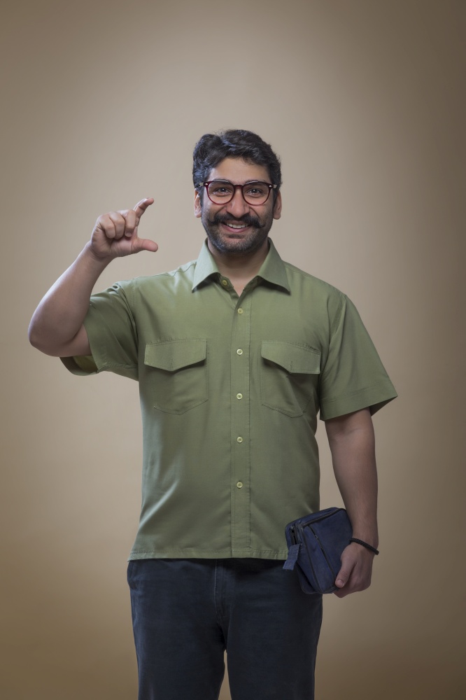 Smiling man wearing eyeglasses holding a small bag in one hand and showing gesture of holding a product with fingers.