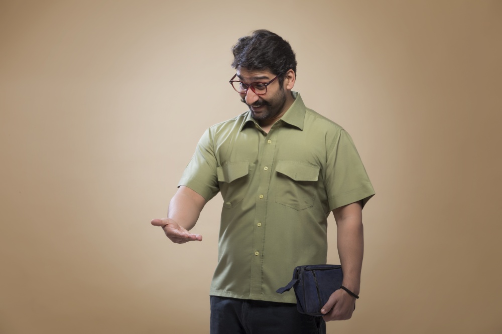 Man wearing eyeglasses holding a small bag in one hand and looking at his palm in surprise.