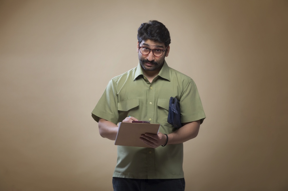 Man wearing eyeglasses writing notes on a pad carrying a small bag.