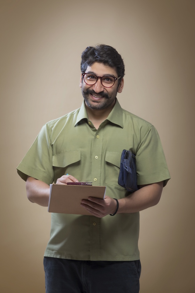 Smiling man wearing eyeglasses writing notes on a pad carrying a small bag.
